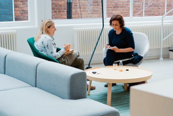 two woman sits on sofa chairs inside house