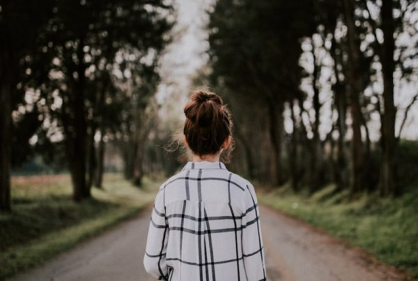 tilt-shift lens photography of woman standing on gray road surrounded with trees