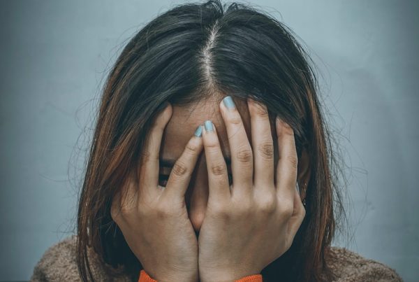 woman in brown sweater covering her face with her hand