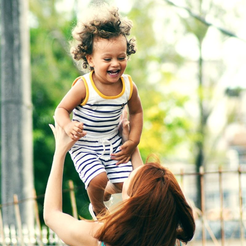 selective focus photo of woman lifting child during daytime