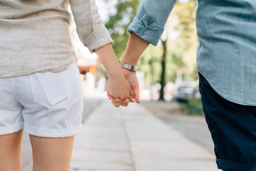 teenage man and woman holding hands together in walkway during daytime